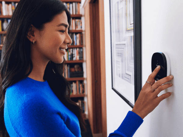 A woman wearing a blue shirt adjusts a thermostat on the living room wall.