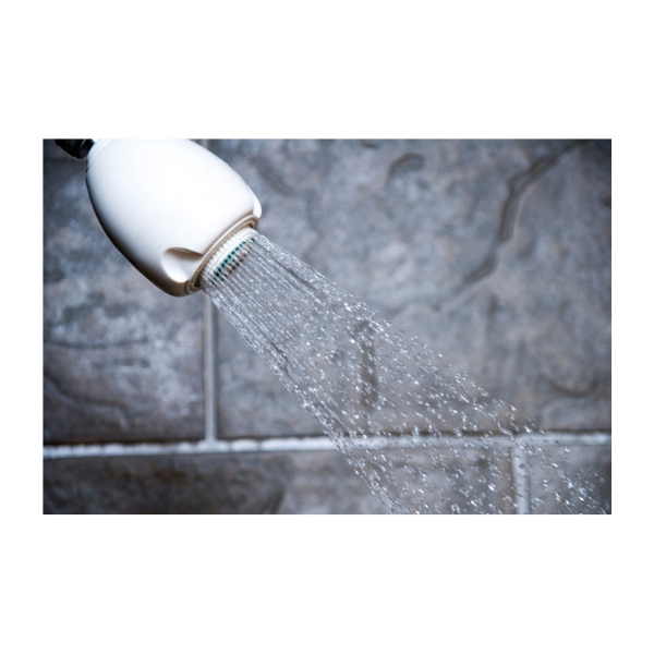 A white showerhead with water flowing. The background is a gray tile wall.