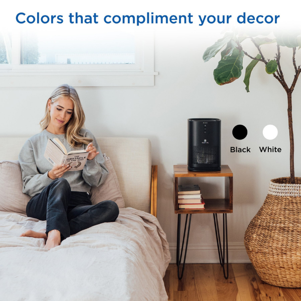 A woman reads next to an air purifier. Text reads Colors that compliment your decor. Black. White.