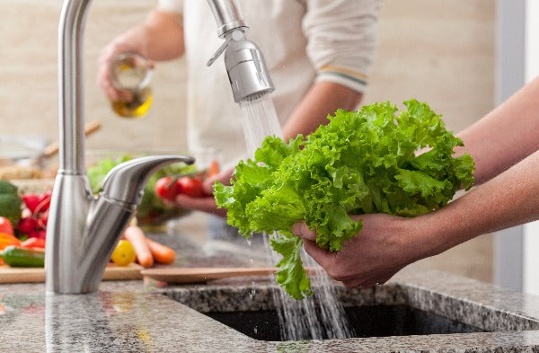 A person washes kale at a kitchen sink using the aerator.
