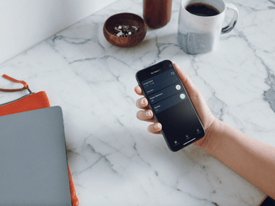 A white person holding a smart phone showing the ecobee app at the kitchen table.